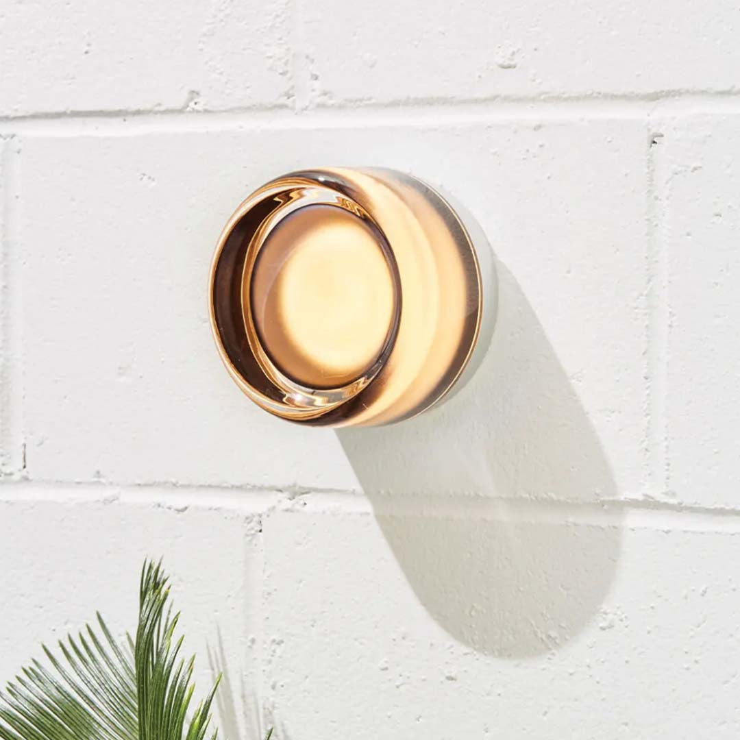 Arden ceramic wall light with a warm amber glow on a white brick wall