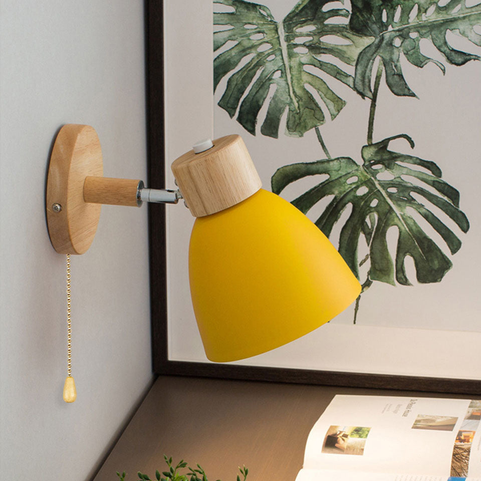 Brindle wooden wall light with a yellow conical shade and pull chain beside a framed print