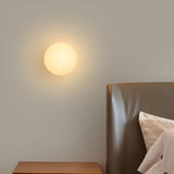 Farleigh round flat wall light glowing softly above a bedside table